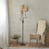 Endon Danemont 3 light floor lamp in matt black with wavy stems holding three tapered hand-wrapped raffia shades, styled in a boho corner setting.