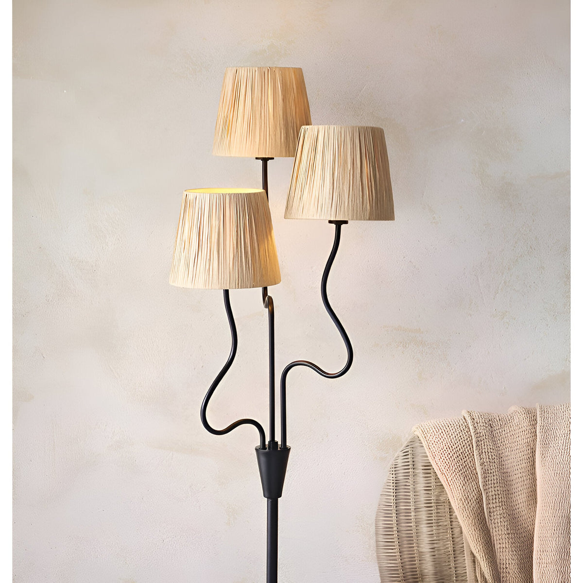 Endon Danemont 3 light floor lamp with wavy matt black arms and tapered hand-wrapped raffia shades, styled beside a woven basket in a neutral room.
