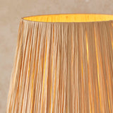 Close-up of the Endon Danemont floor lamp's tapered raffia shade in natural woven finish, glowing warmly against a neutral backdrop.