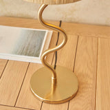 Endon Danemont table lamp close-up showing the brushed brass wavy stem and round base on a wooden floor beside a magazine.
