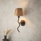 Endon Danemont wall light with a wavy matt black arm and natural raffia tapered shade, mounted on a textured beige plaster wall beside dried pampas grass.