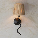 Endon Danemont wall light with wavy matt black arm and hand-wrapped natural raffia shade, mounted on a textured cream wall.