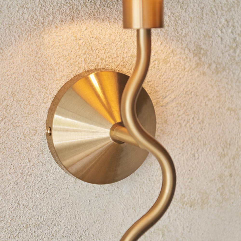 Danemont Wall Light in brass, close-up of the circular cone-shaped backplate and curved metal arm, mounted on a textured plaster wall.