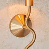 Danemont Wall Light in brass, close-up of the circular cone-shaped backplate and curved metal arm, mounted on a textured plaster wall.