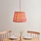 Endon Brackmont Ikat Coral pendant light with handmade pleated tapered faux silk shade in pink and red, on a red braided cable, above a wooden dining table.