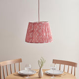 Endon Brackmont Ikat Coral pendant with handmade pleated faux silk shade in pink print and red braided cable, hanging above a wooden dining table.