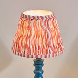 Endon Aldworth Ripple table lamp with turned blue spindle base and pleated coral pink ripple-print fabric shade, illuminated against a neutral background.