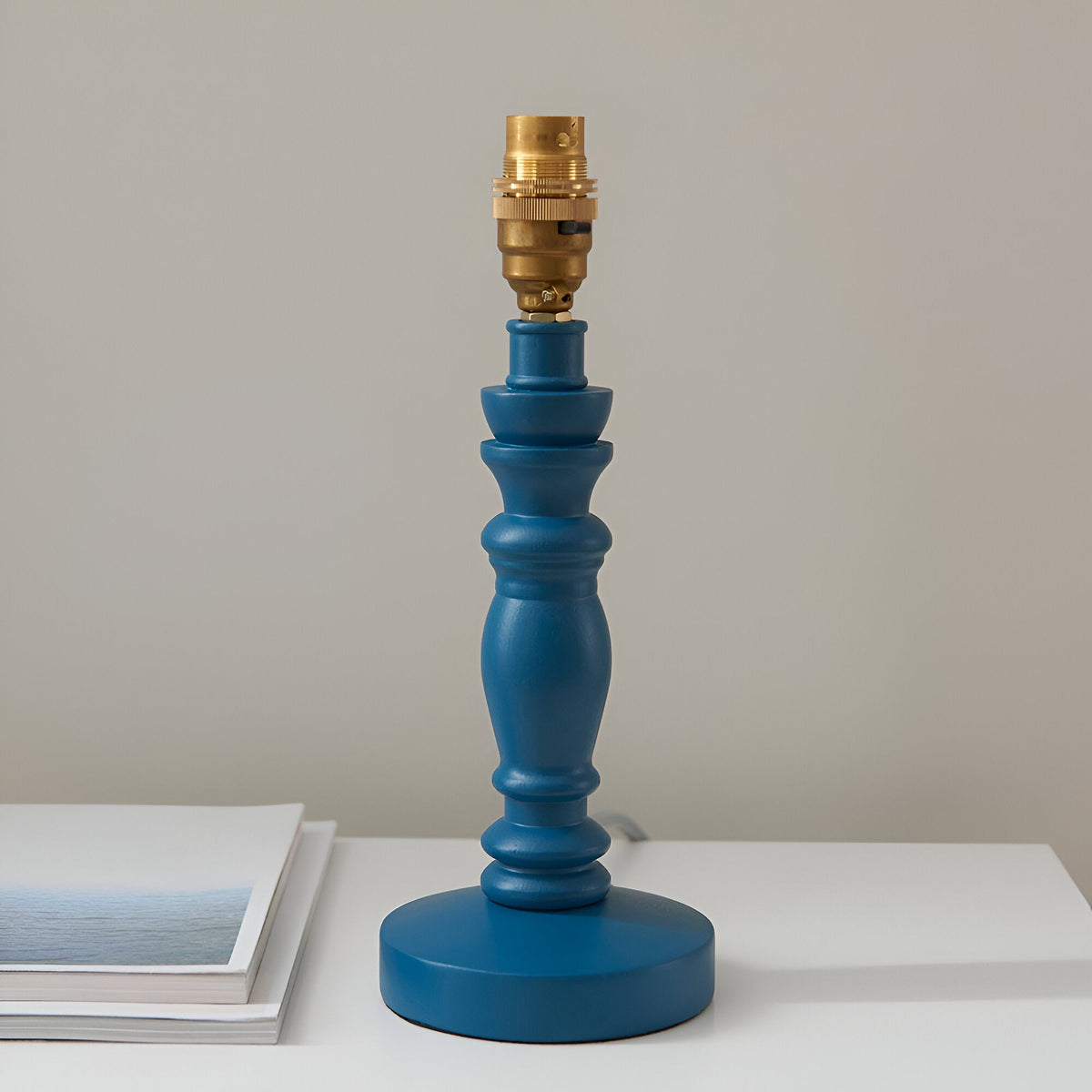 Endon Aldworth Ripple table lamp with turned marlin blue wooden spindle base and brass B22 switched lampholder, shown on a white surface beside a book.