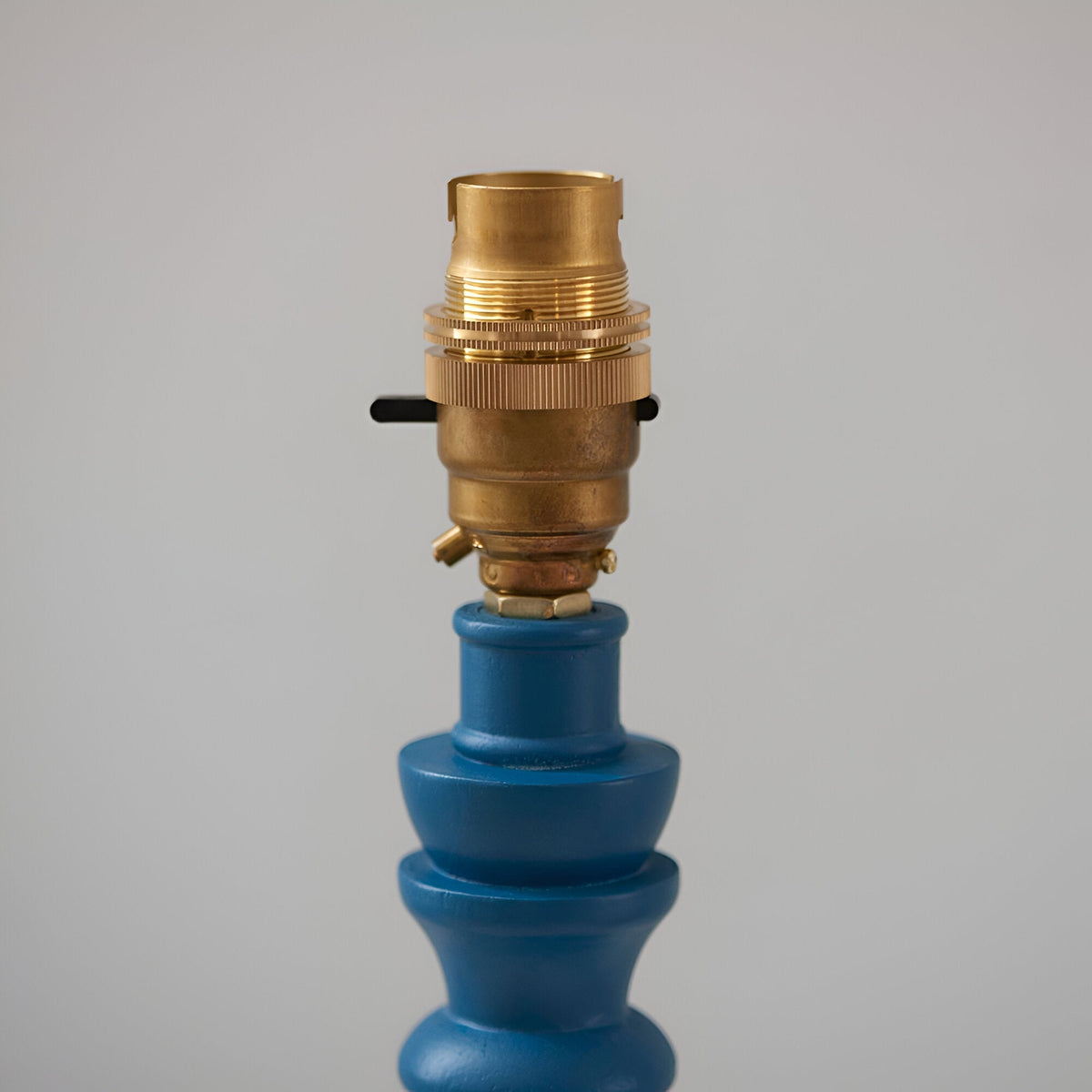 Close-up of the Endon Aldworth Ripple table lamp showing the brass B22 switched lampholder atop a satin blue turned wooden spindle base.