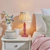 Endon Aldworth Leaf table lamp with pink clay turned spindle base and pleated green leaf-print shade, on a white bedside drawer beside ceramics and bedding.