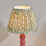 Endon Aldworth Leaf table lamp with a pleated green leaf-print shade on a turned pink clay wooden spindle base, illuminated against a neutral background.