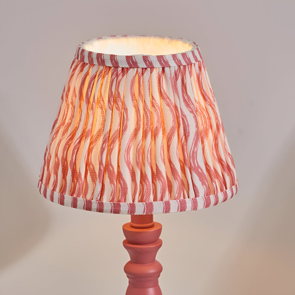 Aldworth Ripple table lamp with pink turned spindle base and pleated ripple-print shade in coral, pink and white stripes, shown on a plain light background.