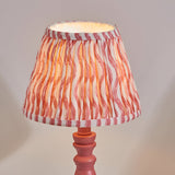Aldworth Ripple table lamp with pink turned spindle base and pleated ripple-print shade in coral, pink and white stripes, shown on a plain light background.