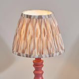 Endon Aldworth Ikat table lamp with pleated natural and grey ikat print shade on a pink turned wooden spindle base, illuminated against a neutral background.