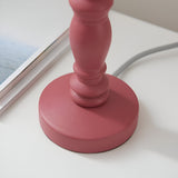 Close-up of the pink clay turned wooden spindle base of the Endon Aldworth Ikat table lamp on a white surface beside a magazine.