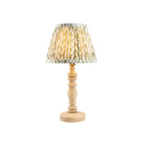Aldworth Leaf table lamp with a turned natural ash spindle base and a pleated leaf-print shade in soft green and cream tones, shown on a plain white background.