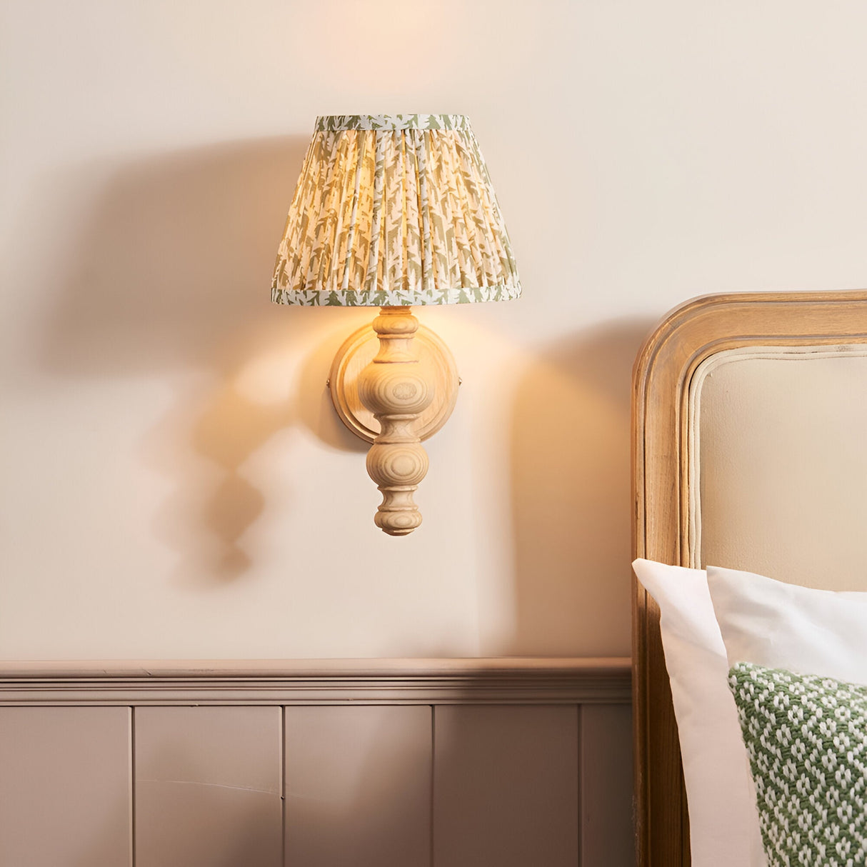 Endon Aldworth Leaf wall light with turned natural ash spindle and pleated herb green leaf-print shade, mounted above a wooden bed headboard.
