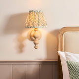 Endon Aldworth Leaf wall light with turned natural ash spindle and pleated herb green leaf-print shade, mounted above a wooden bed headboard.