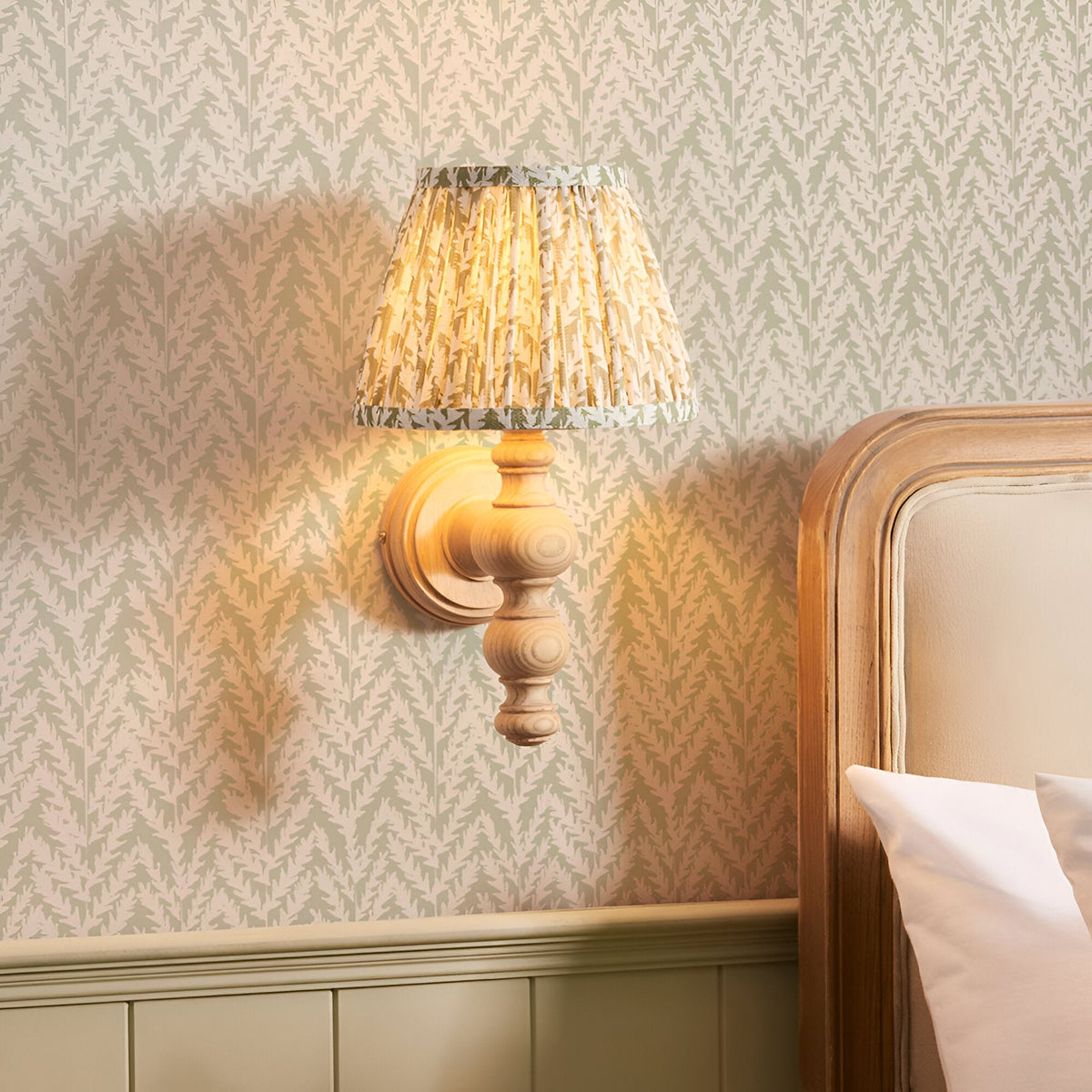 Endon Aldworth Leaf wall light with turned ash spindle and pleated herb green leaf-print shade, mounted on matching leaf wallpaper beside a bed.