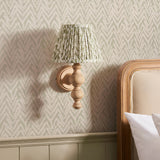 Endon Aldworth Leaf wall light with turned ash spindle and pleated herb green leaf-print shade, mounted on matching wallpaper beside a wooden headboard.