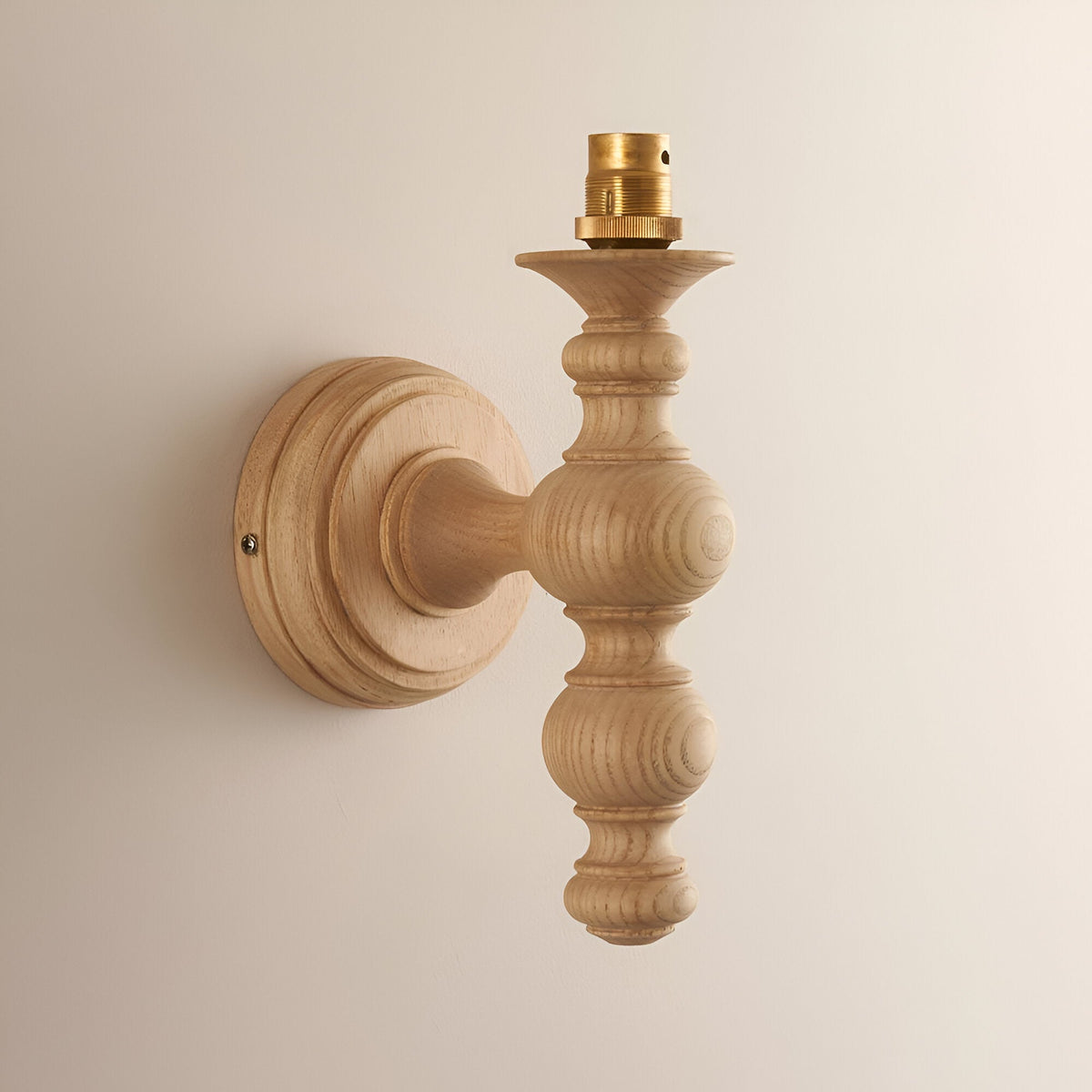 Aldworth Ivy Wall Light in natural ash wood with turned spindle design, brass B22 lamp holder, round wall mount, shown on a plain light background.
