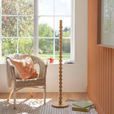 Ashwood Zigzag Floor Lamp in grey with stacked wooden sphere base, shown unshaded in a living room beside a wicker chair and window.