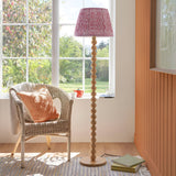Endon Ashwood floor lamp with stacked bamboo sphere base and pink Ripple pleated shade, beside a rattan chair in a sunlit living room.