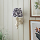 Endon Bevbury Zigzag wall light with almond white turned wood spindle and grey and white pleated zigzag shade, mounted on panelled wall beside botanical prints.