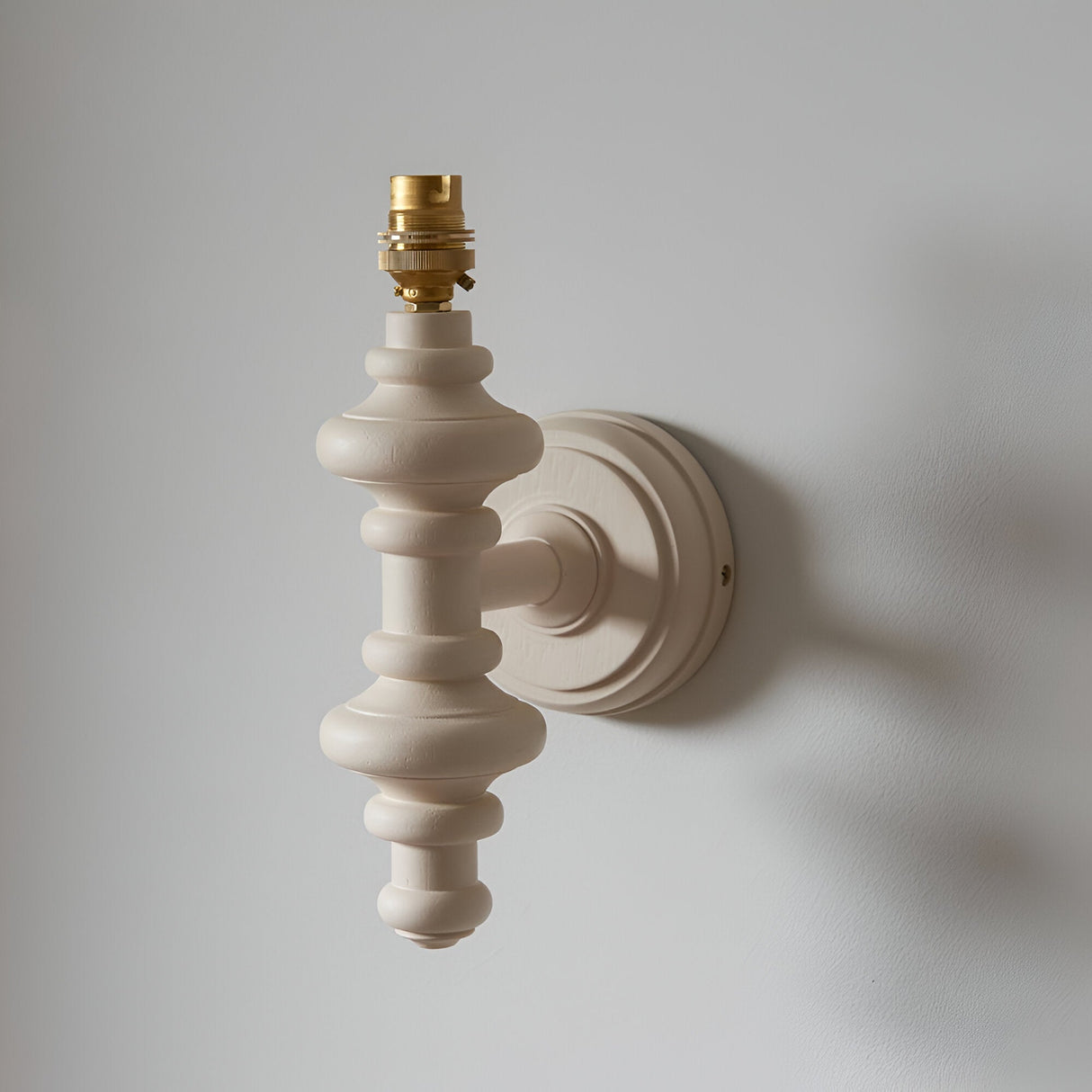 Endon Bevbury Zigzag wall light base in almond white turned wood spindle with brass B22 lamp holder and round backplate, shown against a pale wall.