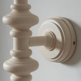 Close-up of the Endon Bevbury Zigzag wall light's turned wooden spindle in satin almond white, mounted on a round backplate against a pale wall.
