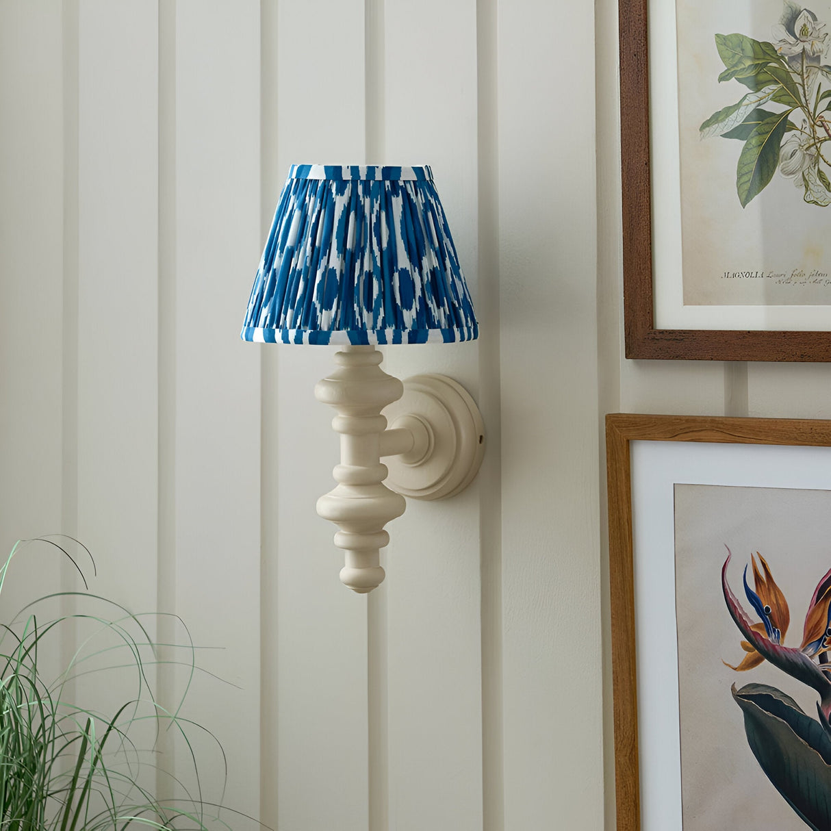 Bevbury Ikat wall light with turned spindle base in off-white and a pleated blue and white patterned shade, mounted on panelled wall near framed prints.
