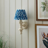 Bevbury Ikat wall light with turned spindle base in off-white and a pleated blue and white patterned shade, mounted on panelled wall near framed prints.