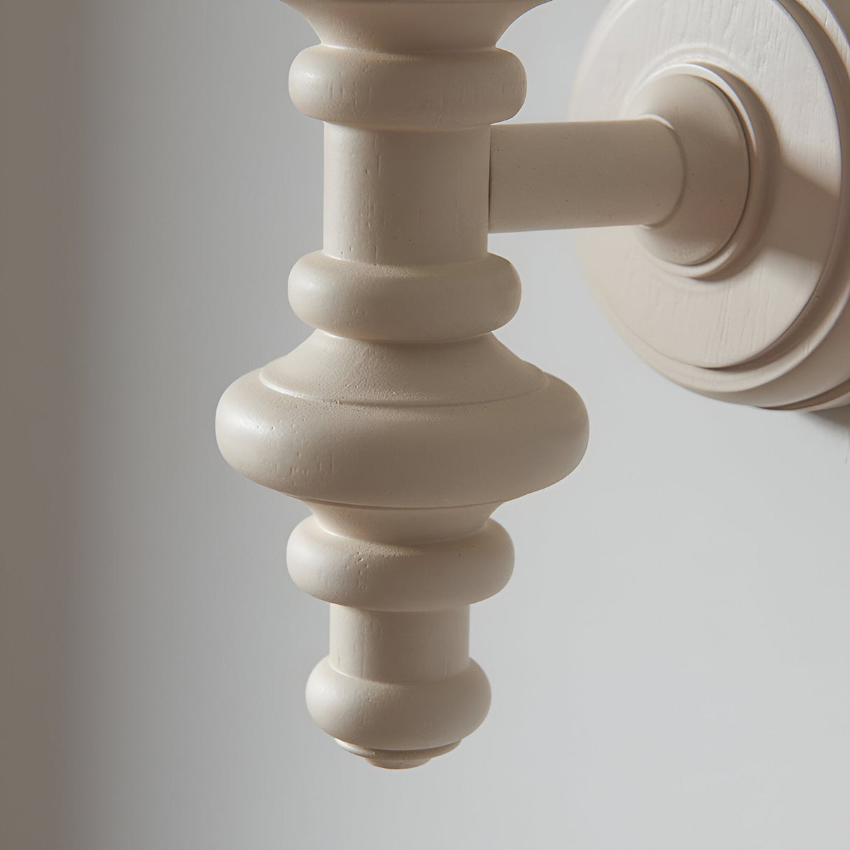 Close-up of the Bevbury Ikat wall light's turned wooden spindle in white, with brass B22 lamp holder and wall-mounted circular backplate.