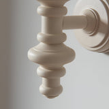 Close-up of the Bevbury Ikat wall light's turned wooden spindle in white, with brass B22 lamp holder and wall-mounted circular backplate.