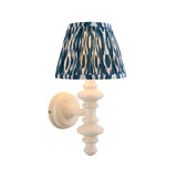 Bevbury Ikat wall light with a turned white spindle base, brass B22 lamp holder, and pleated blue and white Ikat-pattern shade, shown on a plain background.