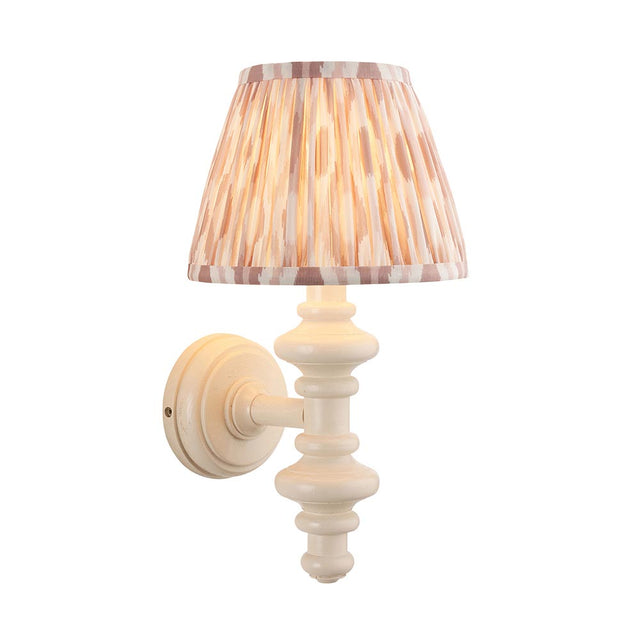 Endon Bevbury Ikat wall light with a white turned wooden spindle, brass B22 lamp holder and tapered pleated Ikat shade in pink and natural tones.