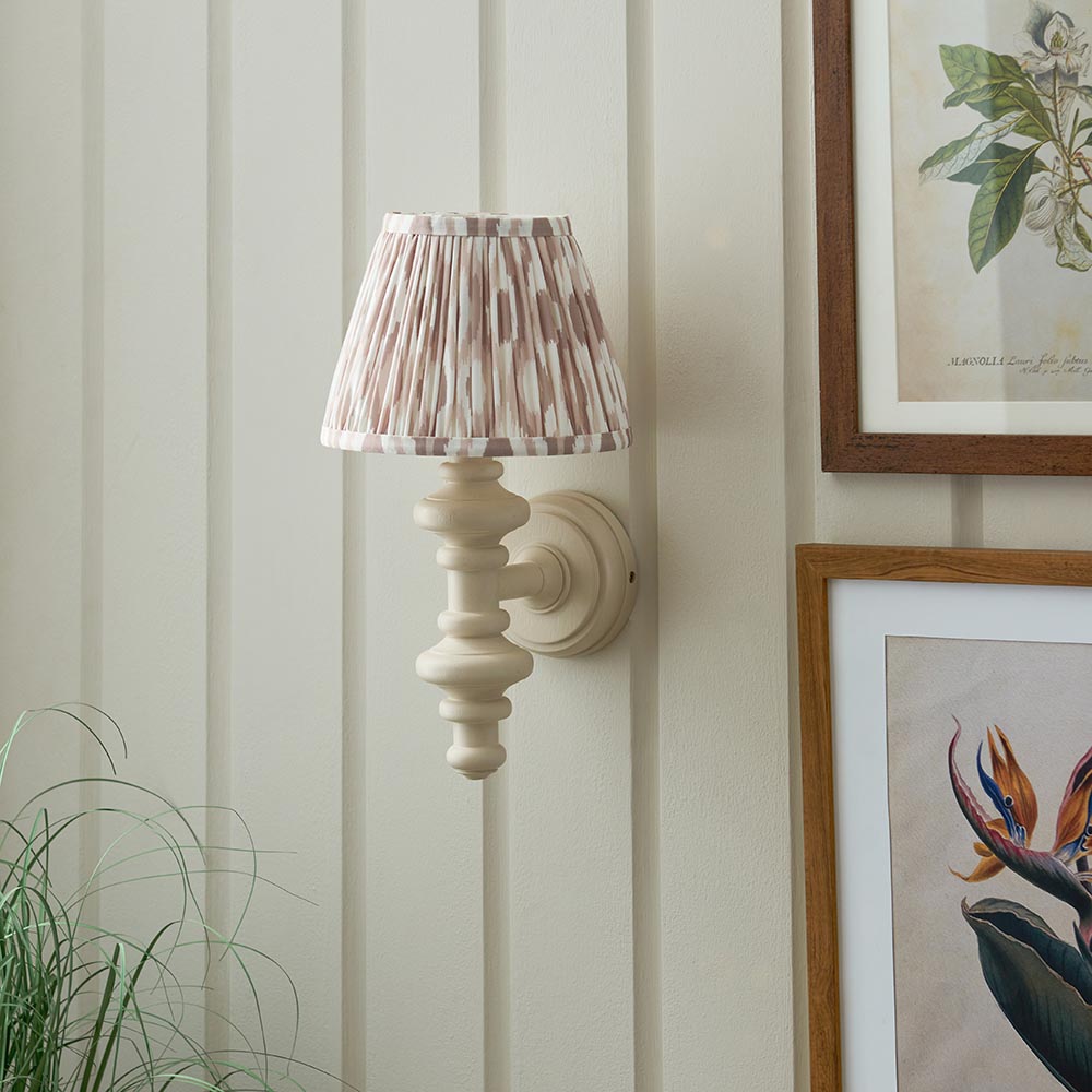 Endon Bevbury Ikat wall light with turned almond white spindle, brass B22 holder and pleated pink ikat shade, mounted on panelled wall beside botanical prints.