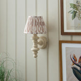 Endon Bevbury Ikat wall light with turned almond white spindle, brass B22 holder and pleated pink ikat shade, mounted on panelled wall beside botanical prints.