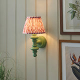 Endon Bevbury Ripple wall light with green turned wooden spindle, brass B22 holder and pink rippled faux linen shade, on panelled wall by botanical prints.