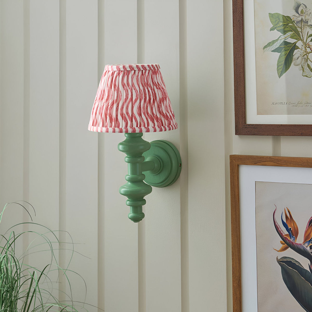 Endon Bevbury Ripple wall light with green turned wood spindle and pink rippled pleated shade, mounted on panelled wall beside framed botanical prints.