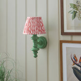 Endon Bevbury Ripple wall light with green turned wood spindle and pink rippled pleated shade, mounted on panelled wall beside framed botanical prints.