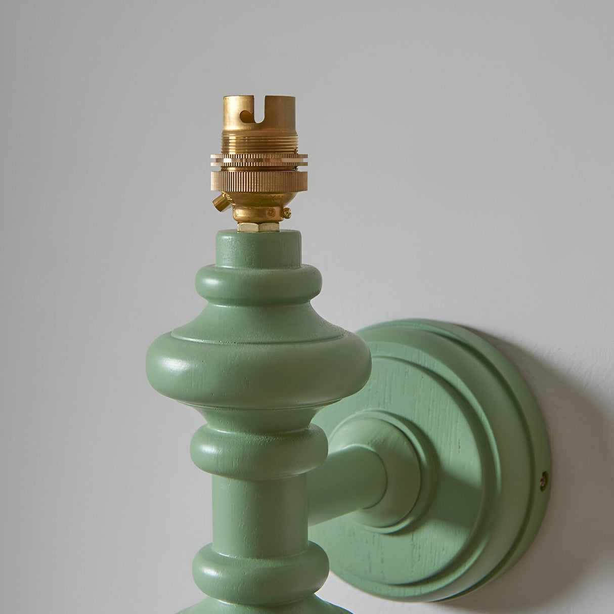 Close-up of the Endon Bevbury Ripple wall light showing the green satin-painted turned wood spindle, brass B22 lamp holder and matching round wall plate.