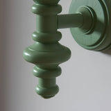 Close-up of the Endon Bevbury Ripple wall light's turned wooden spindle in satin green, mounted on a circular backplate against a pale wall.