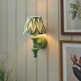 Endon Bevbury Zigzag wall light with green turned wooden spindle and pleated green zigzag faux silk shade, mounted on a panelled wall beside botanical prints.