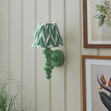 Endon Bevbury wall light with green turned wood spindle and pleated green zigzag faux silk shade, mounted on cream panelled wall by botanical prints.