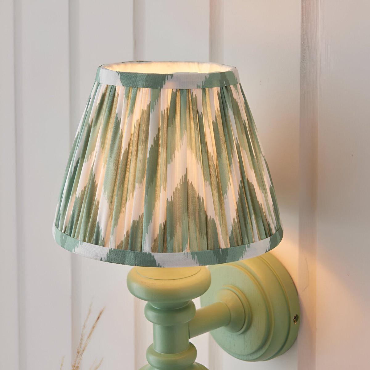 Endon Bevbury Zigzag wall light with a green turned wooden spindle, brass B22 lamp holder, and tapered pleated shade in green and cream zigzag print.