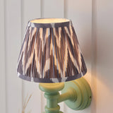 Bevbury Ikat wall light with pleated grey and cream patterned shade on a green turned spindle base, mounted on a panelled wall.