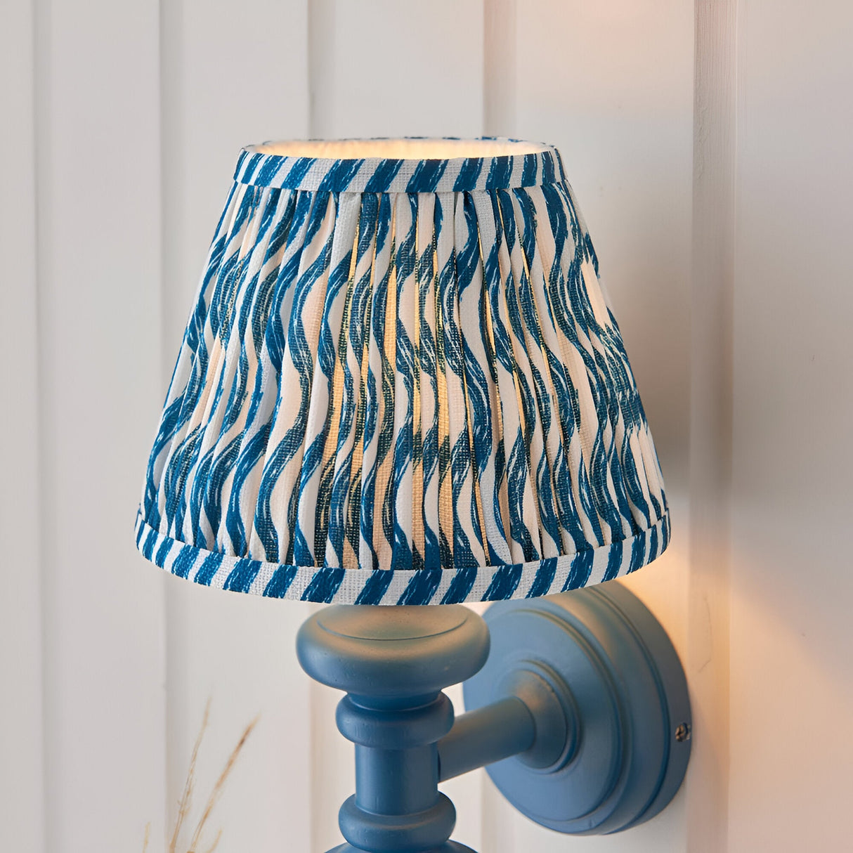 Endon Bevbury Ripple wall light with blue turned wooden spindle, brass B22 holder and tapered pleated shade in blue rippled faux linen print.