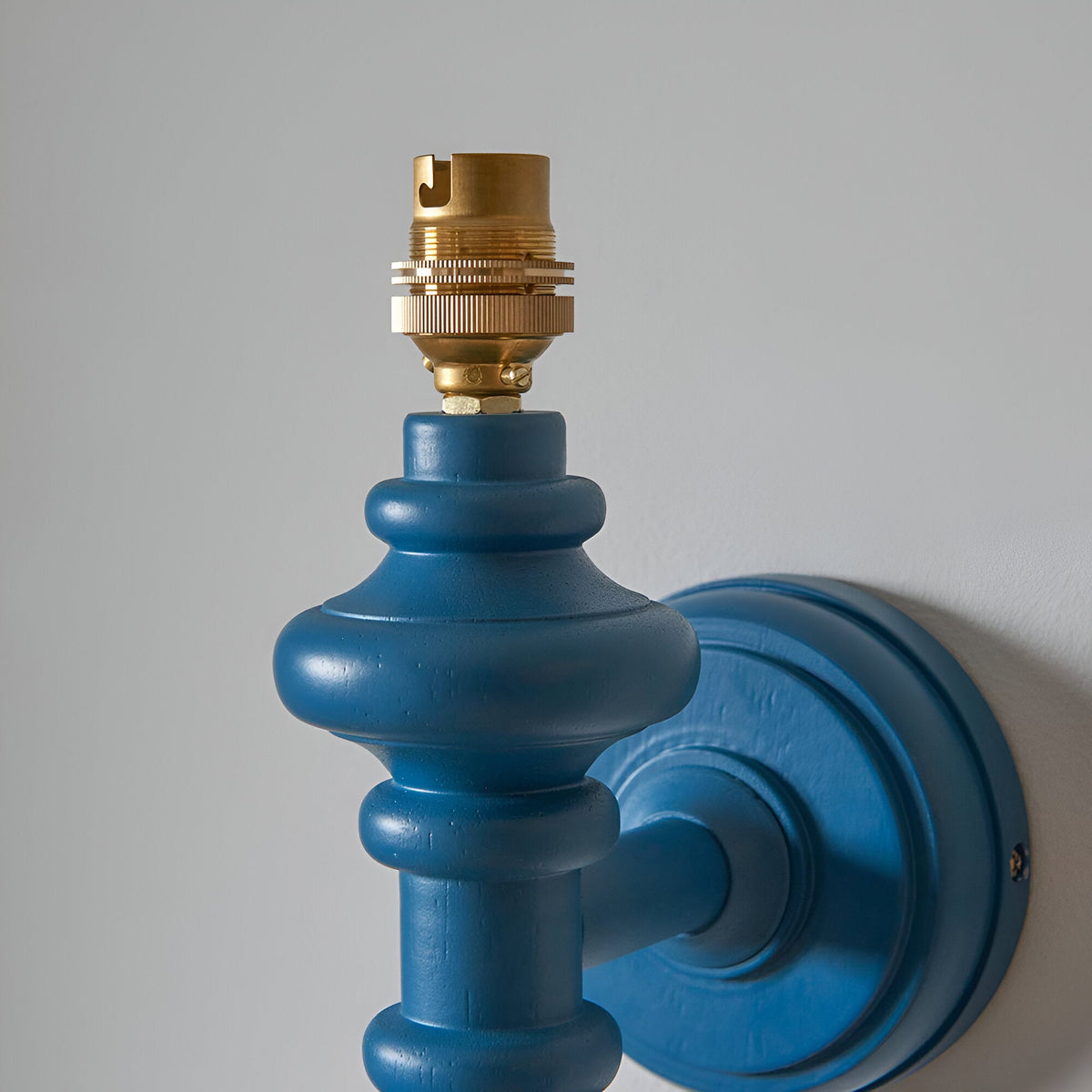 Close-up of the Endon Bevbury Ripple wall light showing the marlin blue turned wooden spindle, brass B22 lamp holder and matching blue circular wall plate.