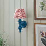 Endon Bevbury Ripple wall light with blue turned wood spindle, brass B22 holder and pink striped faux linen shade, mounted beside framed botanical prints.